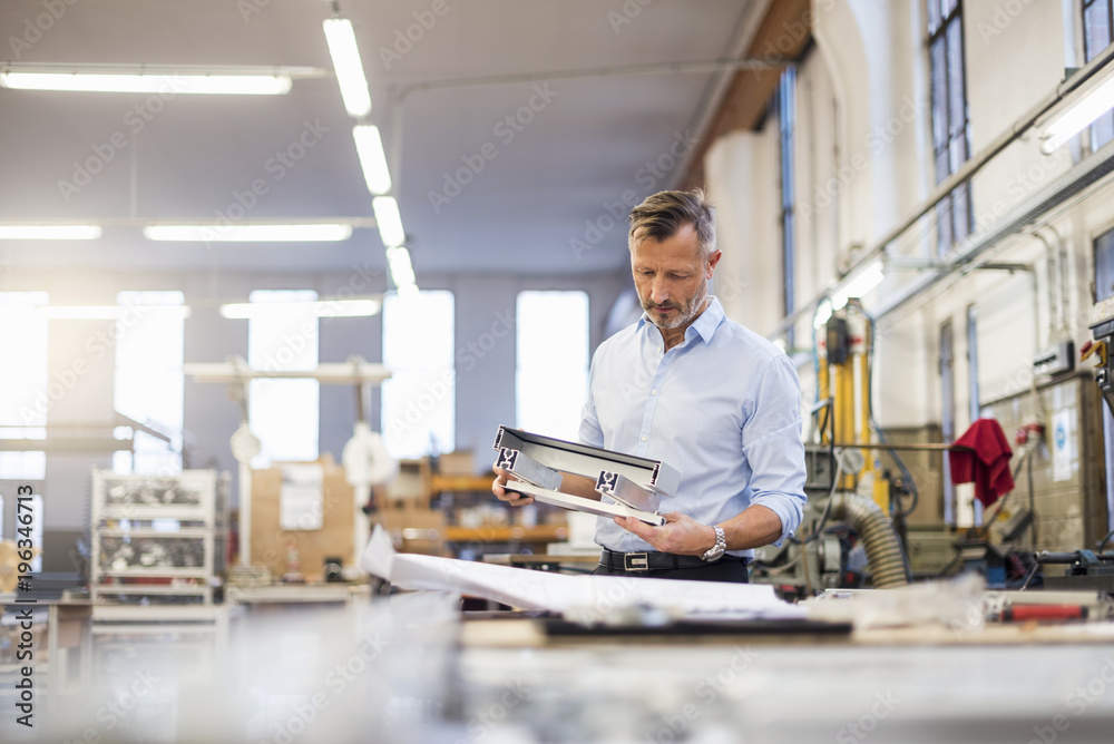 Mature businessman in factory examining component Mature businessman in factory examining component