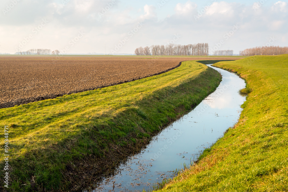 Water surface of a meandering ditch reflects the white clouds in the blue sky