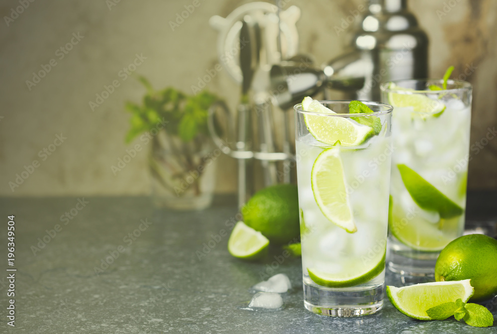 Fototapeta premium Mojito cocktail with lime and mint in glass on a stone table. Bar tools and ingredients for cocktail.