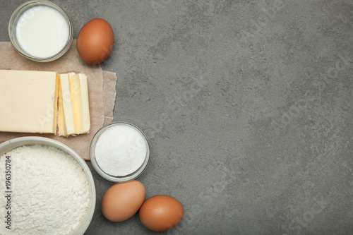 Raw eggs, butter, flour and sugar with milk on a gray background, empty space for text.