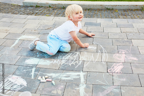 Little boy drawing with chalks on asphalt