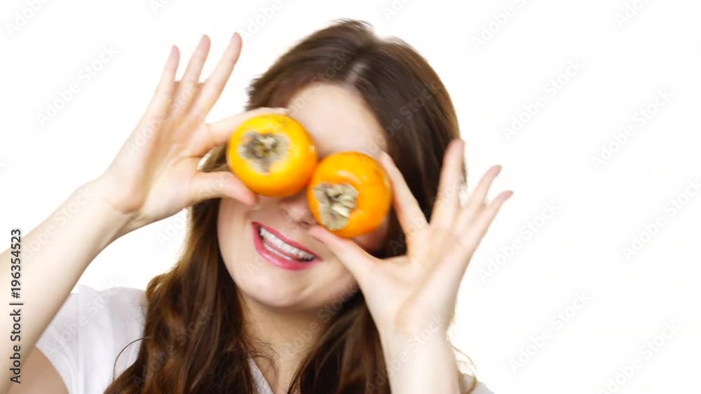 Woman funny brunette girl holding  persimmon kaki fruits on her eyes, playing, isolated on white. Healthy eating, diet, eye health concept