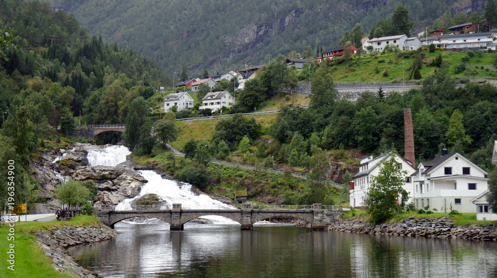 Scenic view of waterfall and bridge in Hellesylt, small town at the entrance to Geirangerfjord on a summer day, mountain in the background, More og Romsdal, Norway