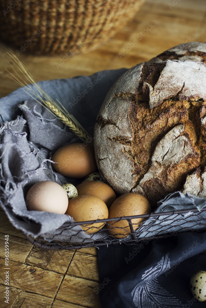 Loaf of rye bread in a basket with chicken eggs on the table Loaf of rye bread in a basket with chicken eggs on the table