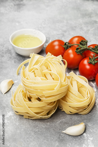 Raw pasta and ingredients for cooking (tomatoes, olive oil, garlic) on gray background