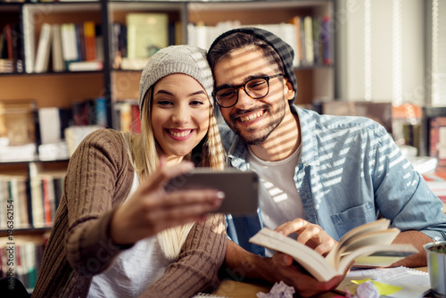 Lovely happy young school love couple taking a selfie while study together in the library.