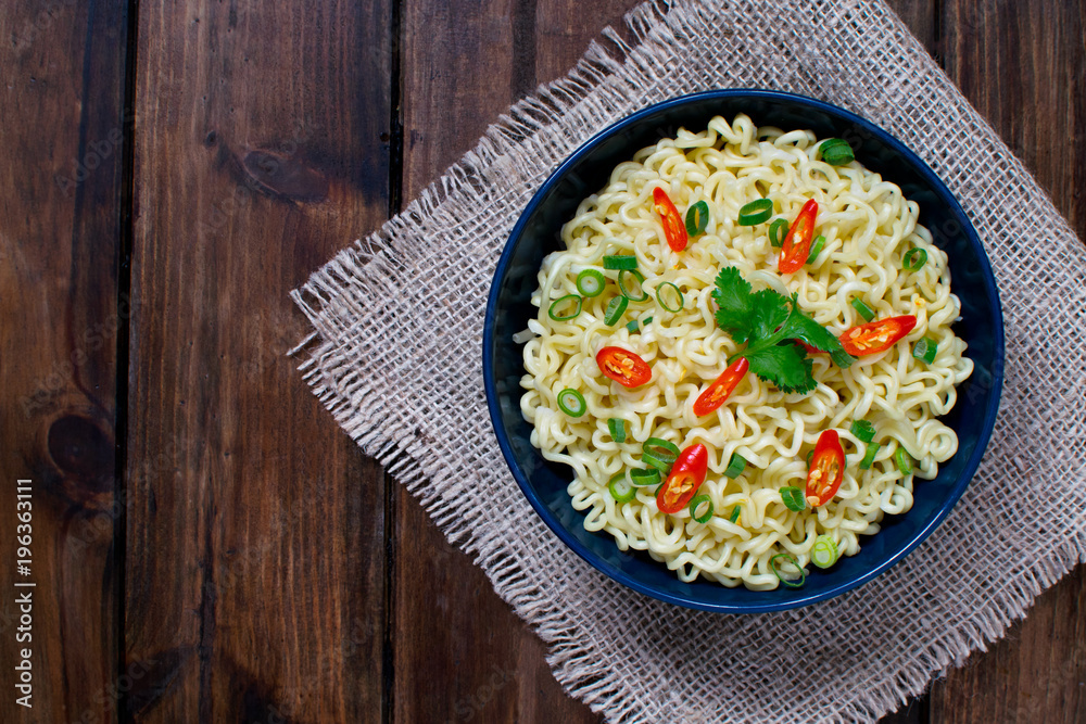 Instant noodles on top with chili ,spring onion and cilantro in dark blue bowl on a sack in wooden background Instant noodles on top with chili ,spring onion and cilantro in dark blue bowl on a sack in wooden background