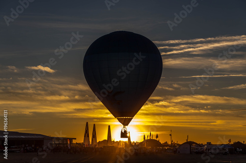 The dark silhouette of hot air balloon rides in the sky against the background of a bright yellow sunset in Spain 