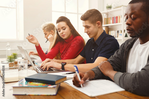 Group of diverse students studying at wooden table