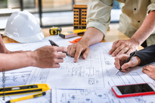 Team engineer meeting for colleagues discussing and checks construction blueprints on new project at desk in office.