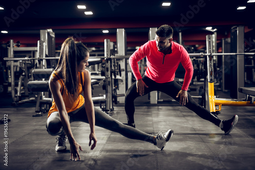 Attractive young shape girl doing workouts with her personal trainer in the modern gym.