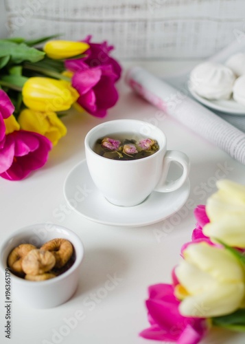 Flat lay with white cup of tea with rose, magazine, marshmallows figs and yellow and pink tulips. Beautiful spring card. Still life