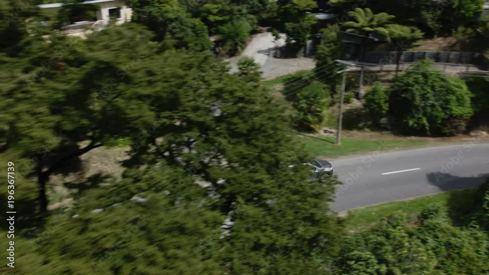 Aerial shot of silver car driving down a country road with green trees overhead. Aerial shot of silver car driving down a country road with green trees overhead.