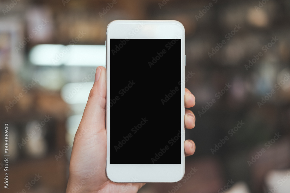 Mockup image of a hand holding white mobile phone with blank black desktop screen with blur background
