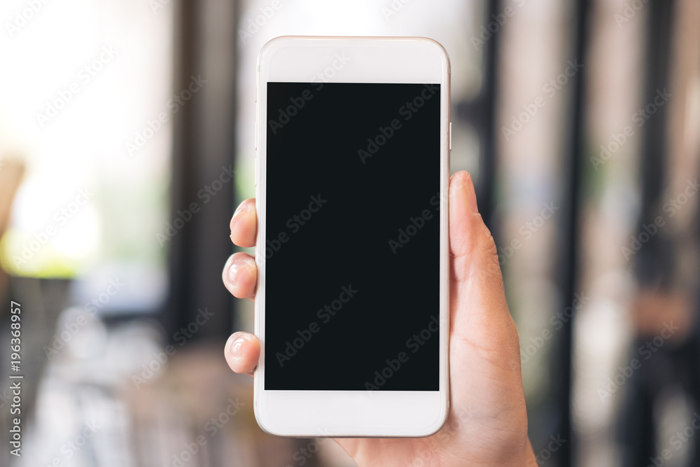 Mockup image of a hand holding white mobile phone with blank black desktop screen with blur background Mockup image of a hand holding white mobile phone with blank black desktop screen with blur background
