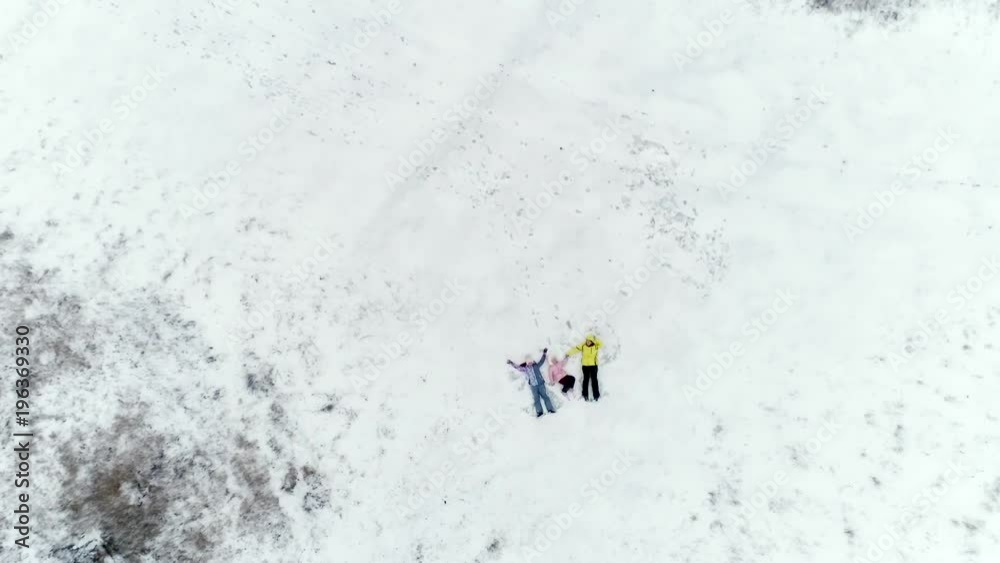 Mom and two daughters making snow angel while lying on snow. Aerial view Mom and two daughters making snow angel while lying on snow. Aerial view