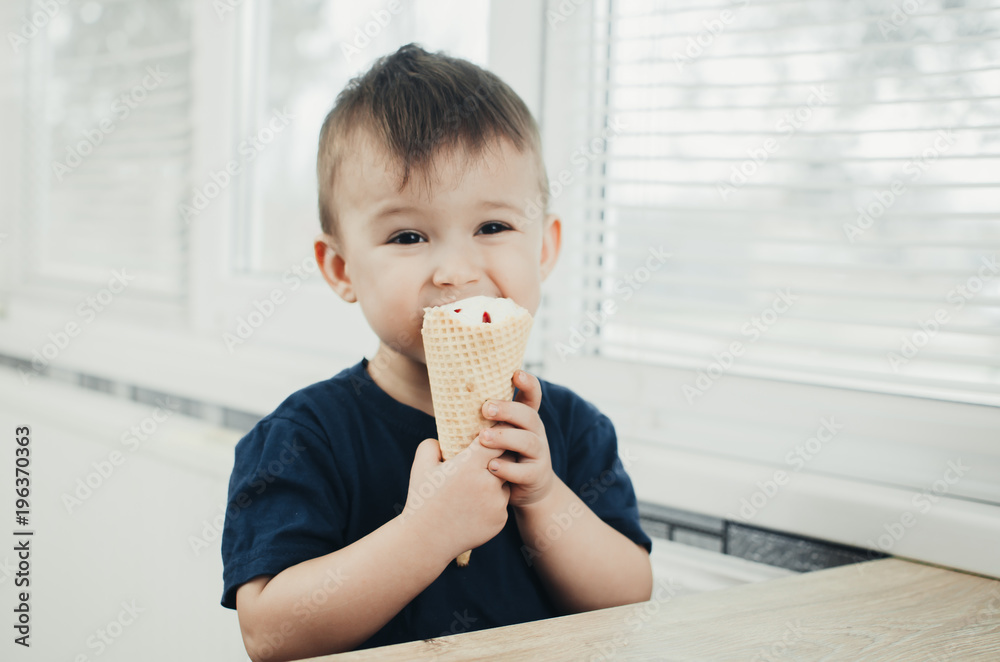 A child in a dark-blue t-shirt in the bright kitchen eating a waffle ice cream cone in the summer house A child in a dark-blue t-shirt in the bright kitchen eating a waffle ice cream cone in the summer house