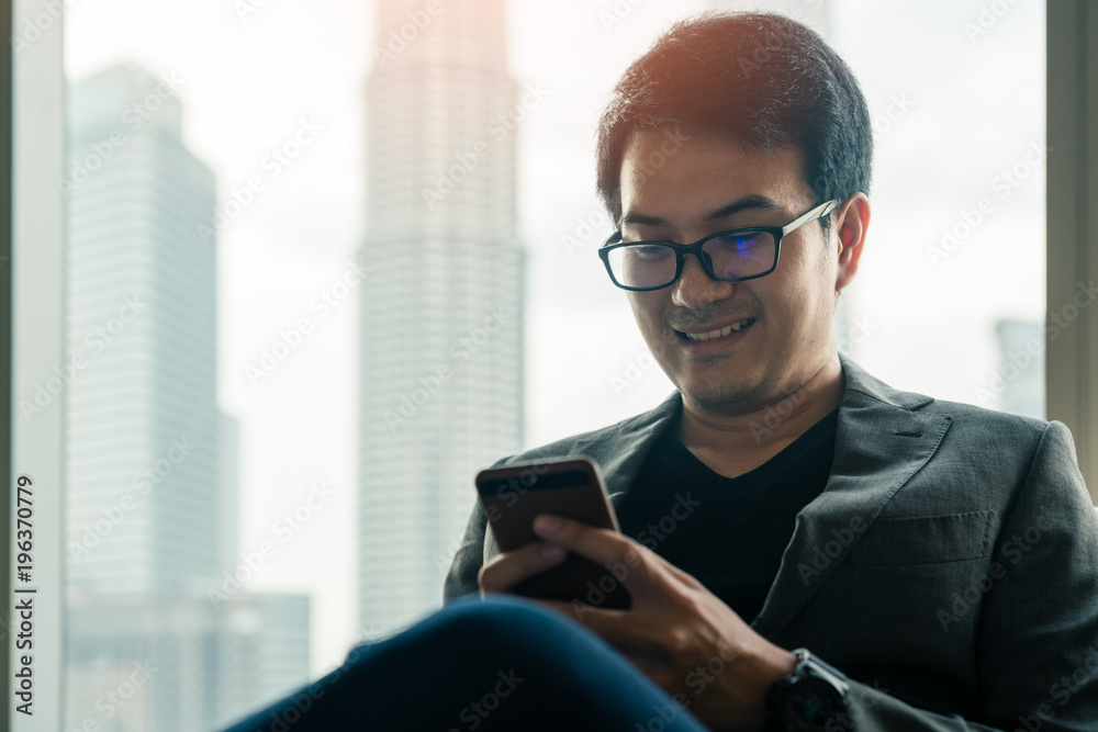 Young asian businessman using smartphone with happiness in hotel with background of cityscape in Kuala Lumpur Panorama at twilight at Kuala Lumpur, Malaysia