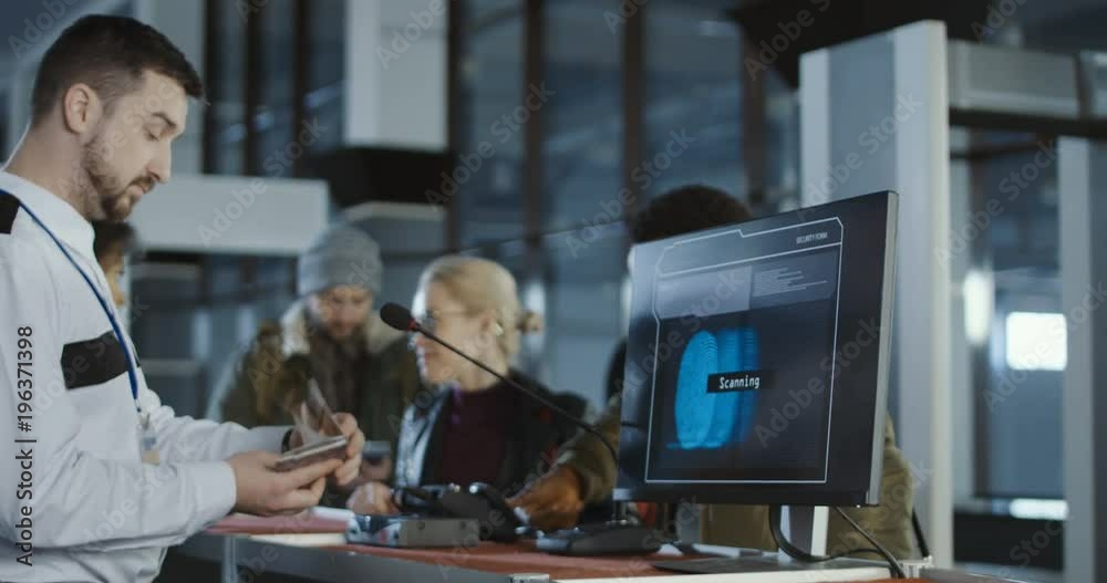Airport security checking a thumb print with a close up view of a computer screen processing the match while two male passengers standing in a queue at the counter behind.