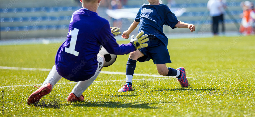 Young soccer goalkeeper save. Boy catching soccer ball. Football bench and children team in the background. Football match for children Young soccer goalkeeper save. Boy catching soccer ball. Football bench and children team in the background. Football match for children