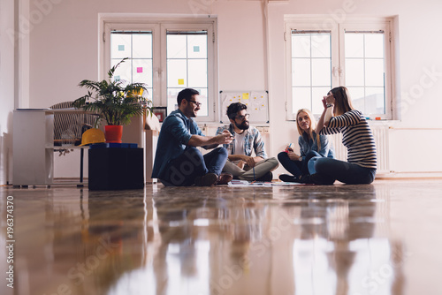 Young hardworking creative business people sitting on the floor of the office in the circle and making a business plan together. Teamwork and togetherness concept.