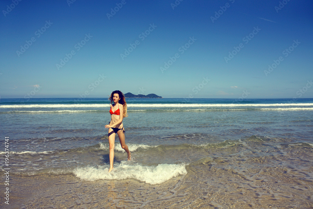 young woman in swimsuit running along the seashore, Brazil