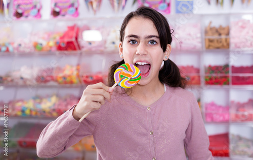 Smiling small girl with lollipop on stick in sweet-shop