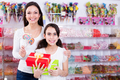 Portrait of mother with daughter standing with lollipop and gifts in store