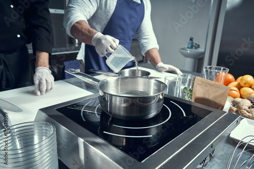 the chef prepares the dish in a frying pan. Hands close-up of chefs. Frying pan on the stove