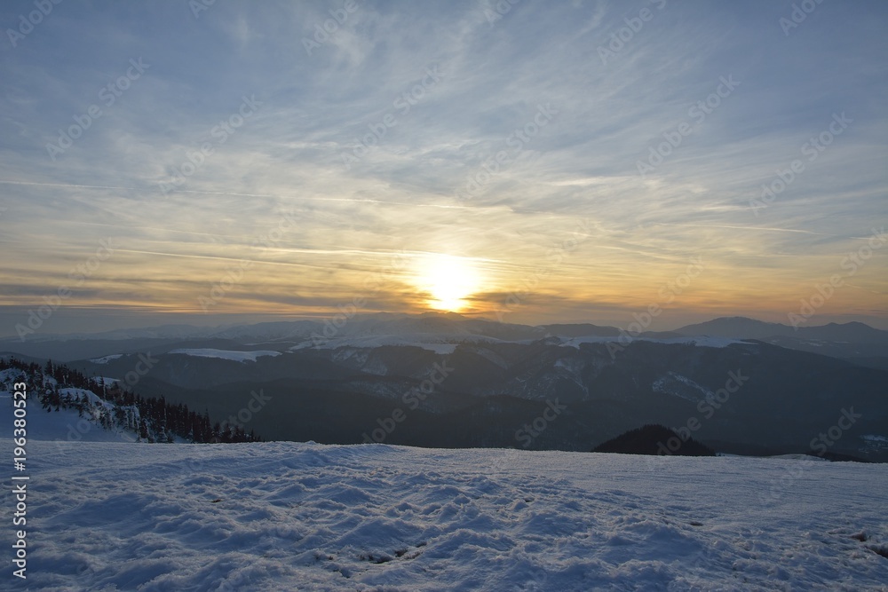 Sunset time in a cloudy day in Ciucas Mountains. The fir forest is covered with snow Sunset time in a cloudy day in Ciucas Mountains. The fir forest is covered with snow