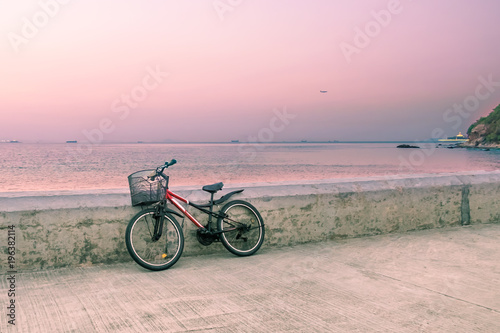 Lonely bicycle with basket standing on concrete pier. Seascape background at sunset golden hour. Toned image.