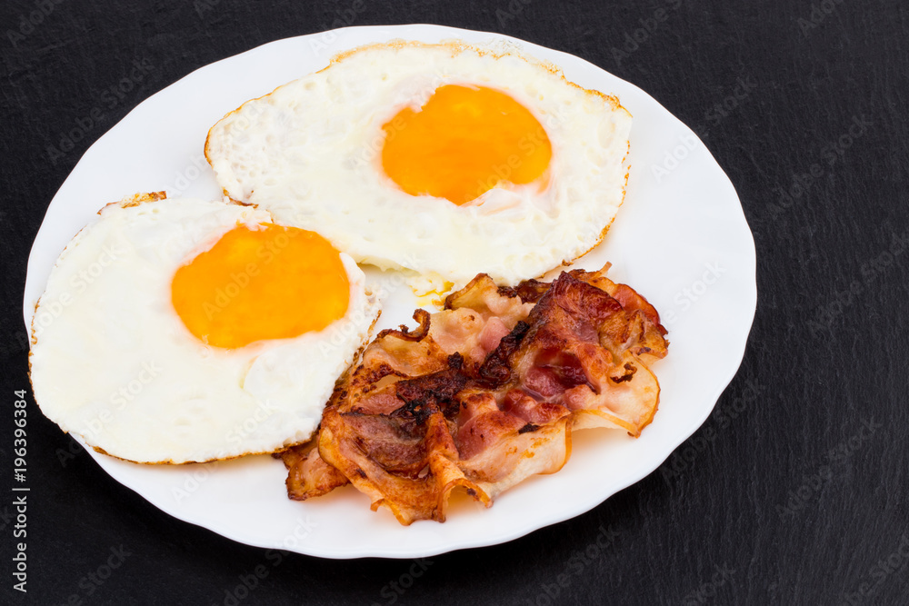 Breakfast with fried eggs and bacon on dark stone background