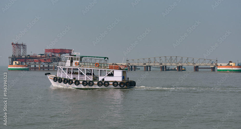 A view of a boat on sea drive & looking a refinery plant at sea at background.