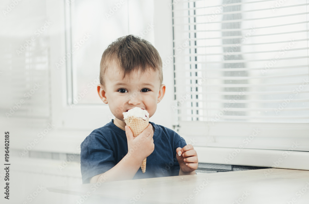 A child in a dark-blue t-shirt in the bright kitchen eating a waffle ice cream cone in the summer house A child in a dark-blue t-shirt in the bright kitchen eating a waffle ice cream cone in the summer house