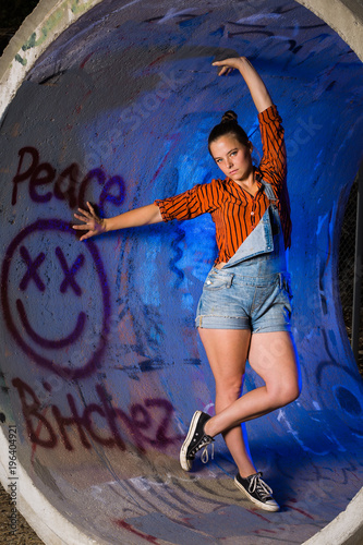 Young mixed race woman dressed in grungy hipster style outdoors poses with colored lights in an industrial area