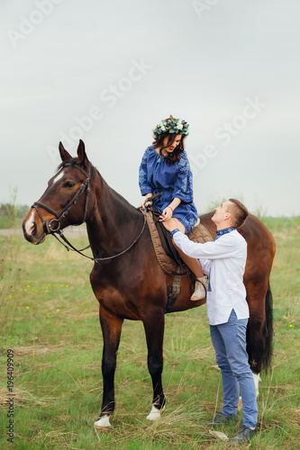 a girl with a wreath on her head sitting on a horse and looking at a man who stands next to her and also looks at her © Ivan