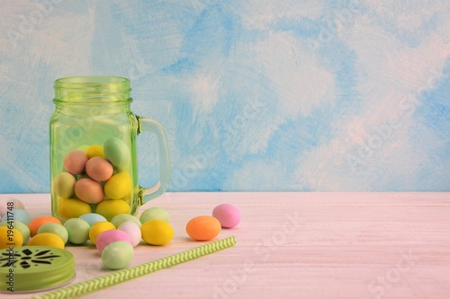 Green transparent glass jar with colored Easter eggs and green straw