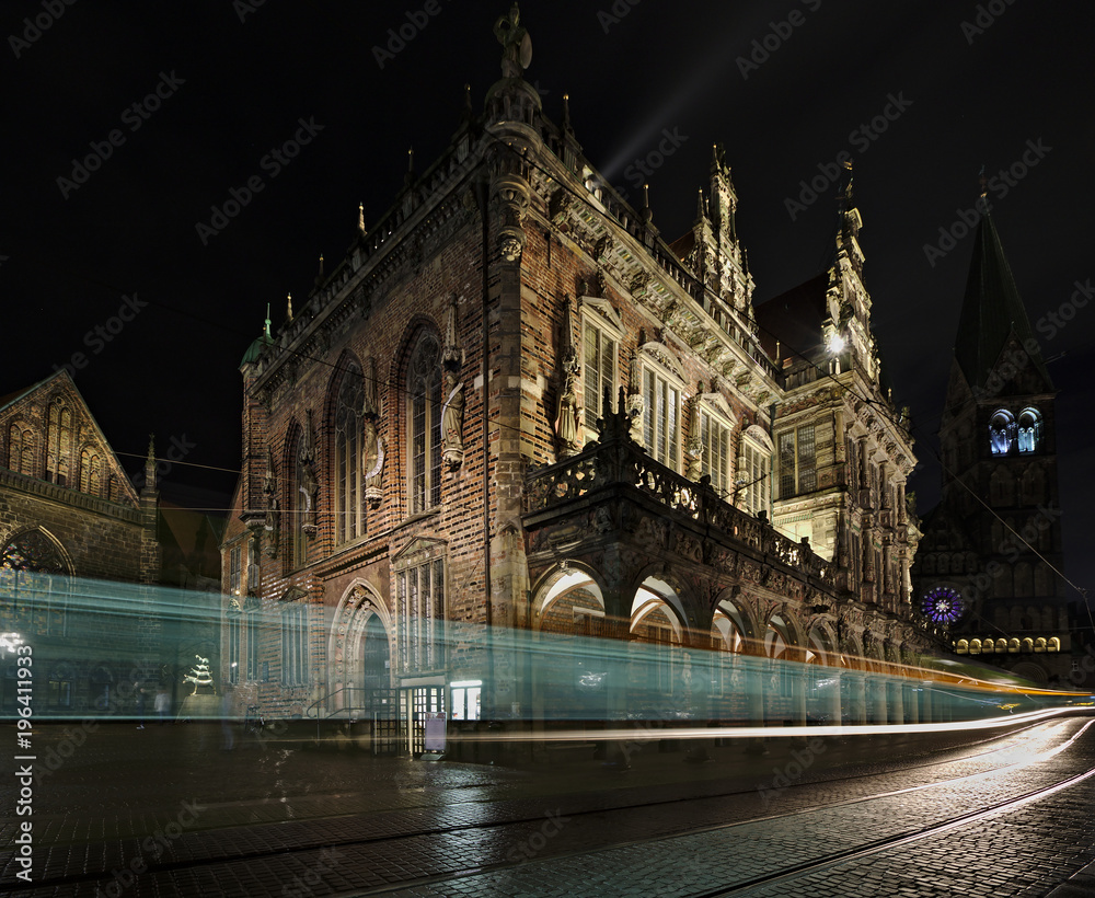 Fototapeta premium Historic city hall in Bremen, Germany at night with St Paul's Cathedral and the Church of our Lady in the background and tram passing by (long exposure)