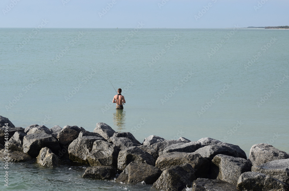 Young man fishing alone in the calm sea, sunny day.