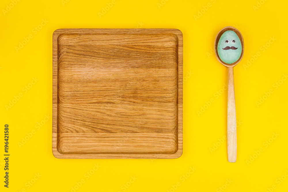 Happy Easter concept. Wooden plates in shape of heart, square with colorful easter eggs with comic face on yellow background Happy Easter concept. Wooden plates in shape of heart, square with colorful easter eggs with comic face on yellow background