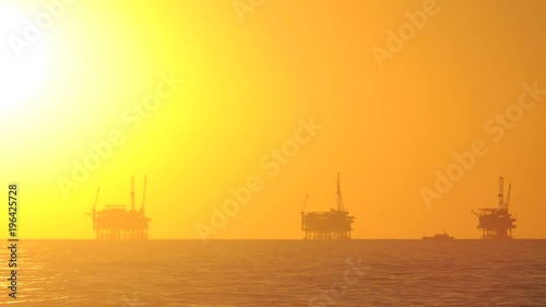 Day to night time lapse of the sun setting behind three oil platforms in the Santa Barbara Channel, California.