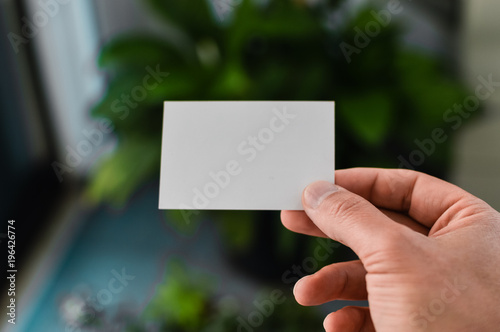 Closeup on hand of a person holding showing white business card over blurry office background