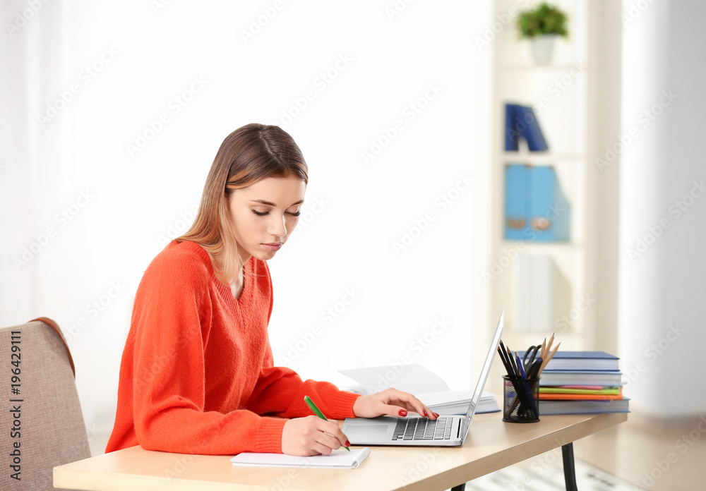 Pretty student with laptop studying at table indoors Pretty student with laptop studying at table indoors