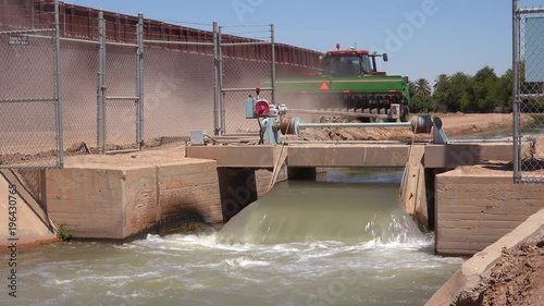 A farmers tractor follows a tributary of the Colorado River as it flows along the border wall between the US and Mexico.