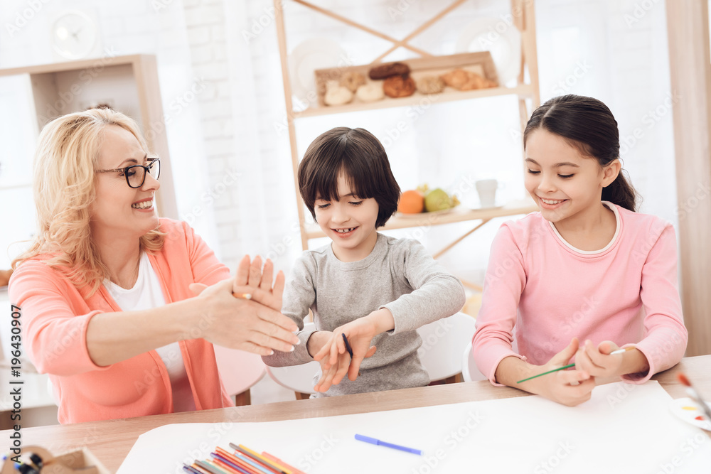 Beautiful elderly woman teaches children to draw. Children draw with paints. Beautiful elderly woman teaches children to draw. Children draw with paints.