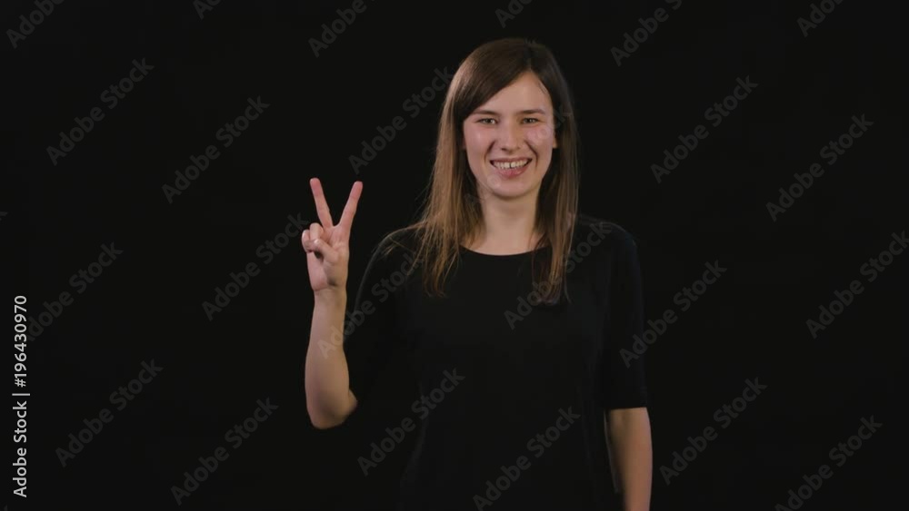 A beautiful young lady showing a Peace gesture against a black background. Medium Shot