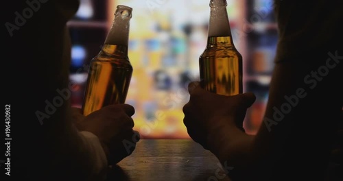 Two guys clink glasses of beer in his hand, bar counter.