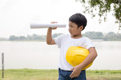 Asian boy in white t-shirt dress like engineer look through roll paper with garden and pond scene