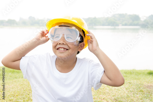 Asian boy in white t-shirt with safety glass and yellow helmet dress like engineer with garden scene
