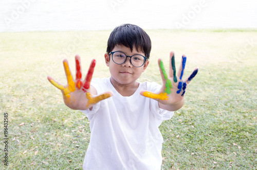 Asian boy in white t-shirt with colorful paint on his fingers with garden scene